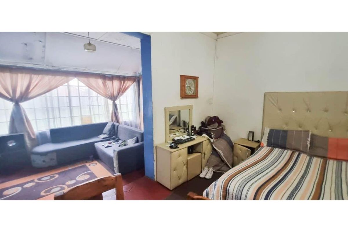 An open-plan living and bedroom area featuring large windows and basic finishes, requiring cosmetic updates to improve the overall aesthetic and condition.