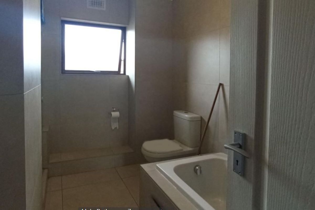 A functional bathroom featuring neutral wall and floor tiles, a built-in bathtub, and a standard toilet.