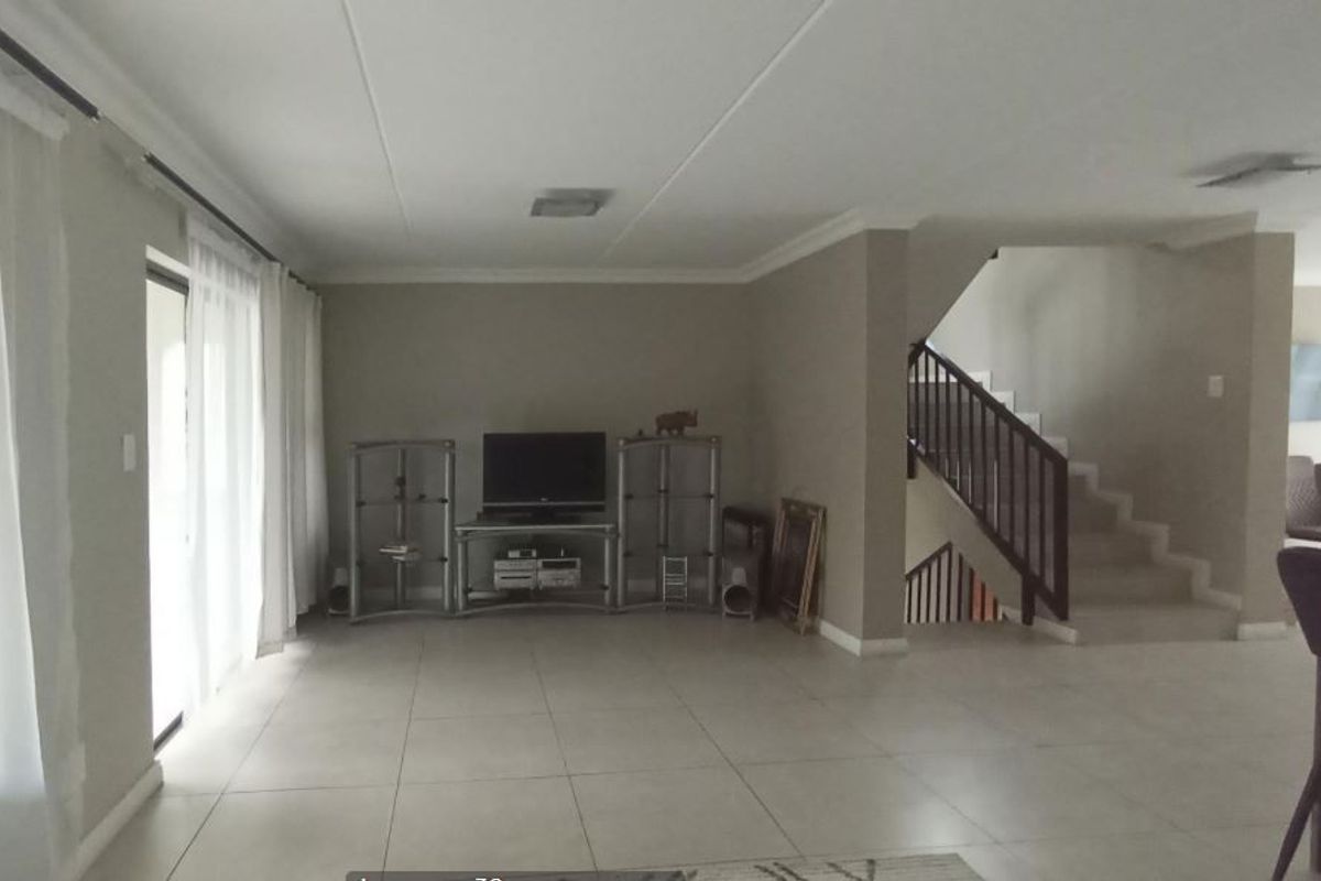 Spacious living area featuring neutral tiled flooring, a staircase with a wooden balustrade, and large sliding glass doors providing access to the exterior.