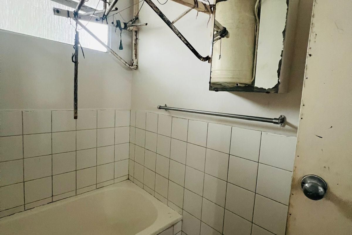 A dated bathroom featuring a built-in bathtub, tiled walls, and a medicine cabinet, requiring significant renovation and modernization of fixtures and finishes.