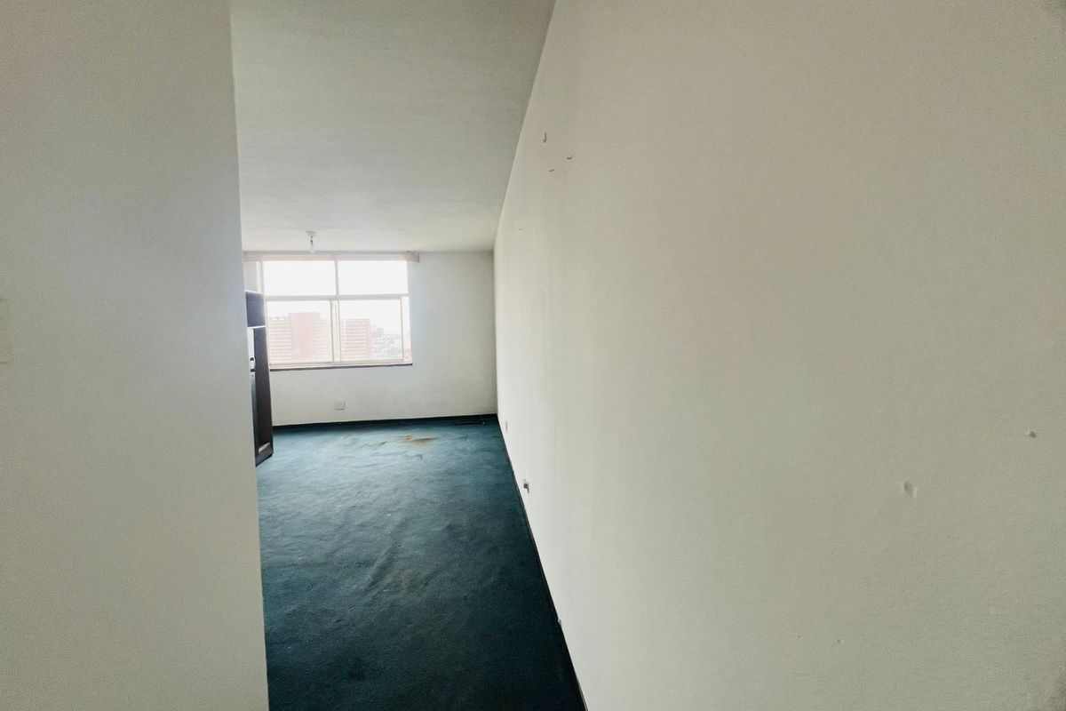 An empty bedroom featuring carpet flooring and a large window, requiring cosmetic updates to the walls and flooring to improve its overall condition.