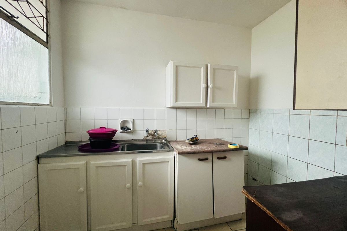 A compact kitchen featuring basic built-in cabinetry, a stainless steel sink, and tiled backsplash, offering a functional space ready for modernization.