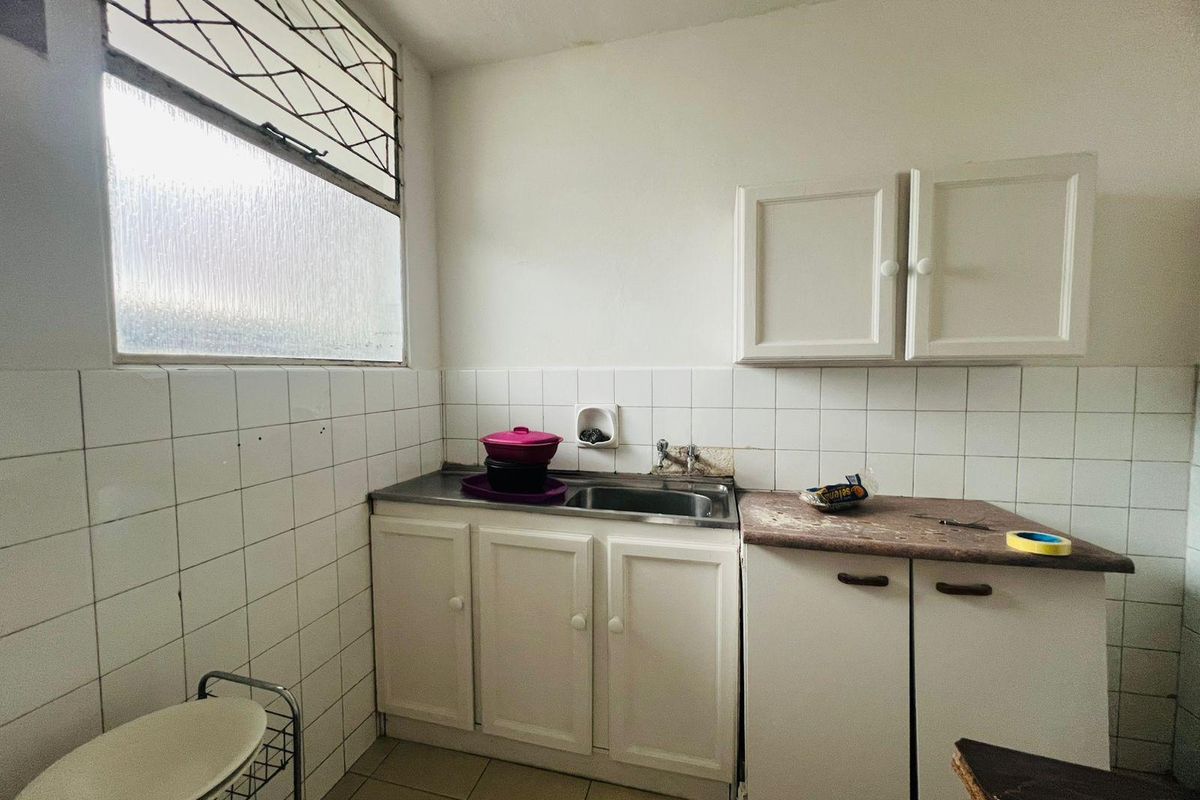 A compact kitchen area featuring built-in white cabinetry, a stainless steel sink, and tiled backsplash, requiring cosmetic updates to improve its overall condition.