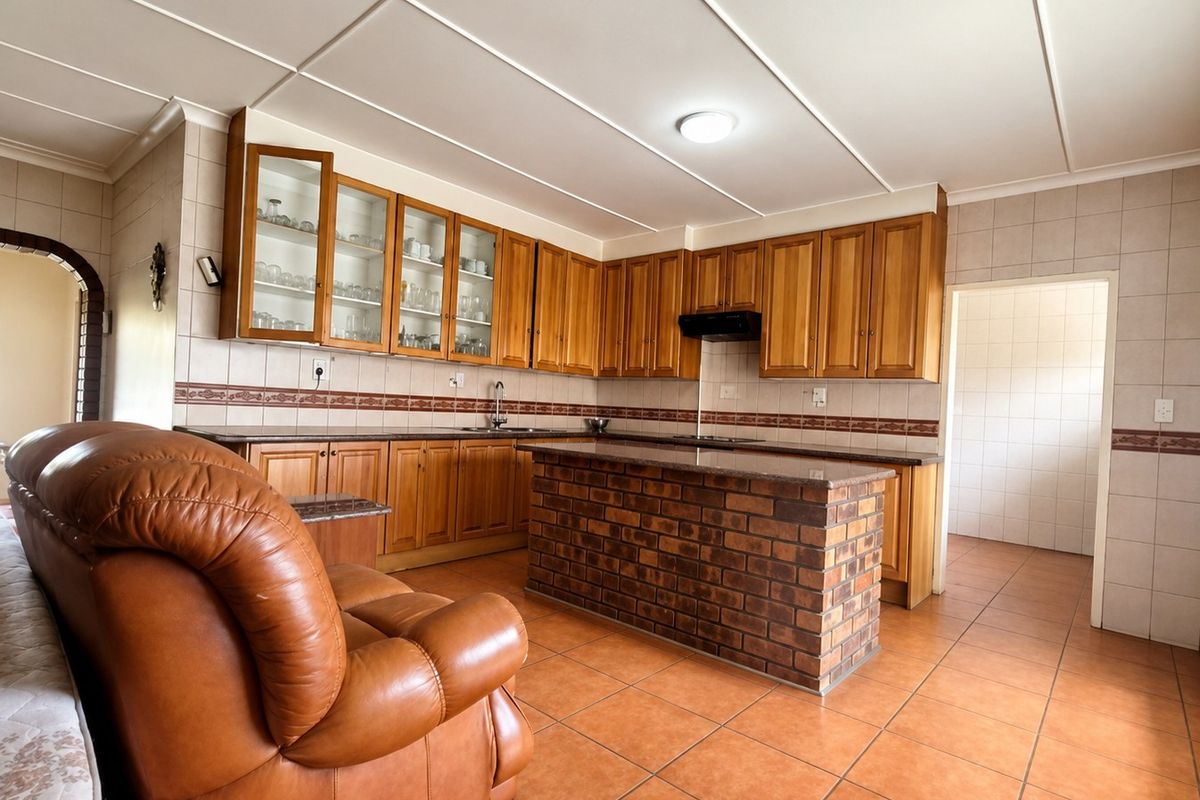 Spacious kitchen featuring wooden cabinetry, granite countertops, a central brick island, and tiled flooring, offering a functional layout with ample storage space.