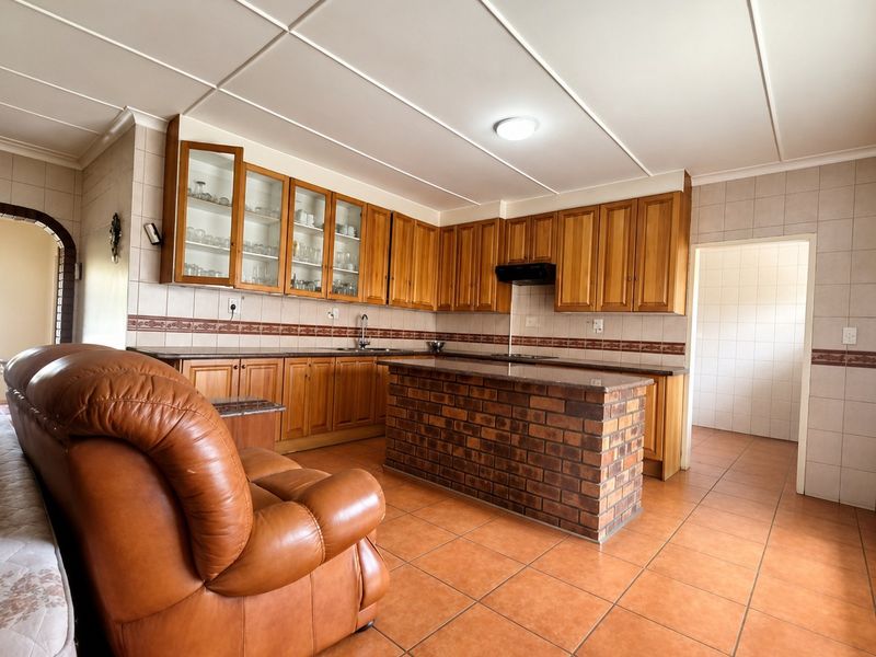 Spacious kitchen featuring wooden cabinetry, granite countertops, a central brick island, and tiled flooring, offering a functional layout with ample storage space.