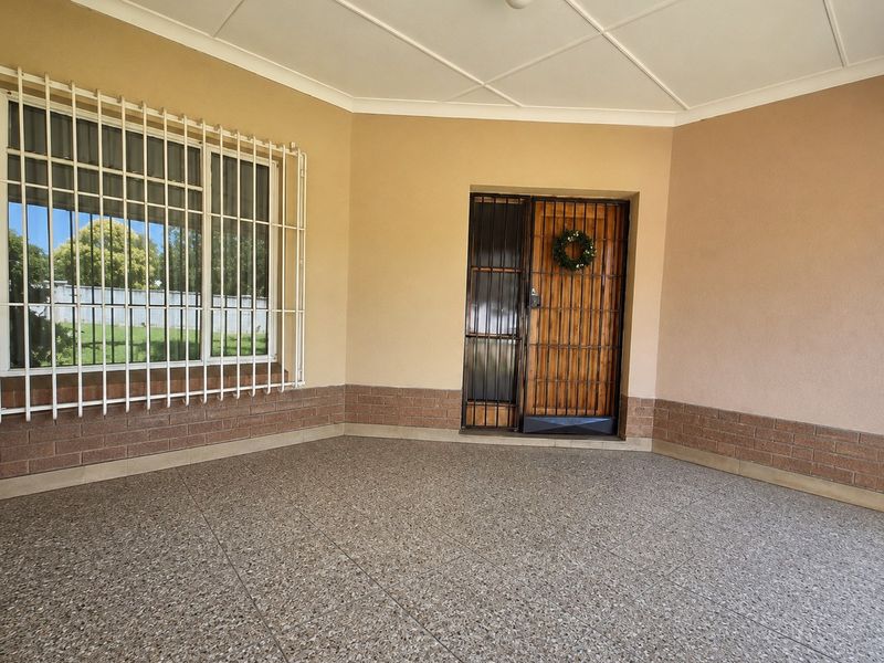 A covered patio area featuring tiled flooring, brick base detailing, and secure entrance access with security gates and window bars.