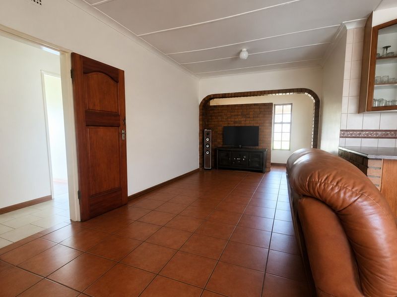 A living room featuring terracotta-style floor tiles, a distinctive exposed brick archway, and a solid timber door leading to an adjacent hallway.