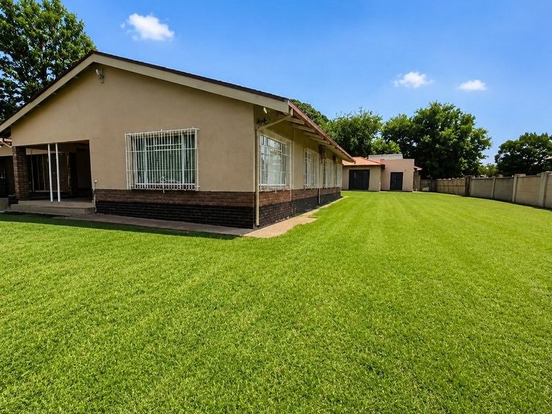 A spacious rear garden featuring a well-maintained lawn, a covered patio area, and secure window bars on the main house structure.