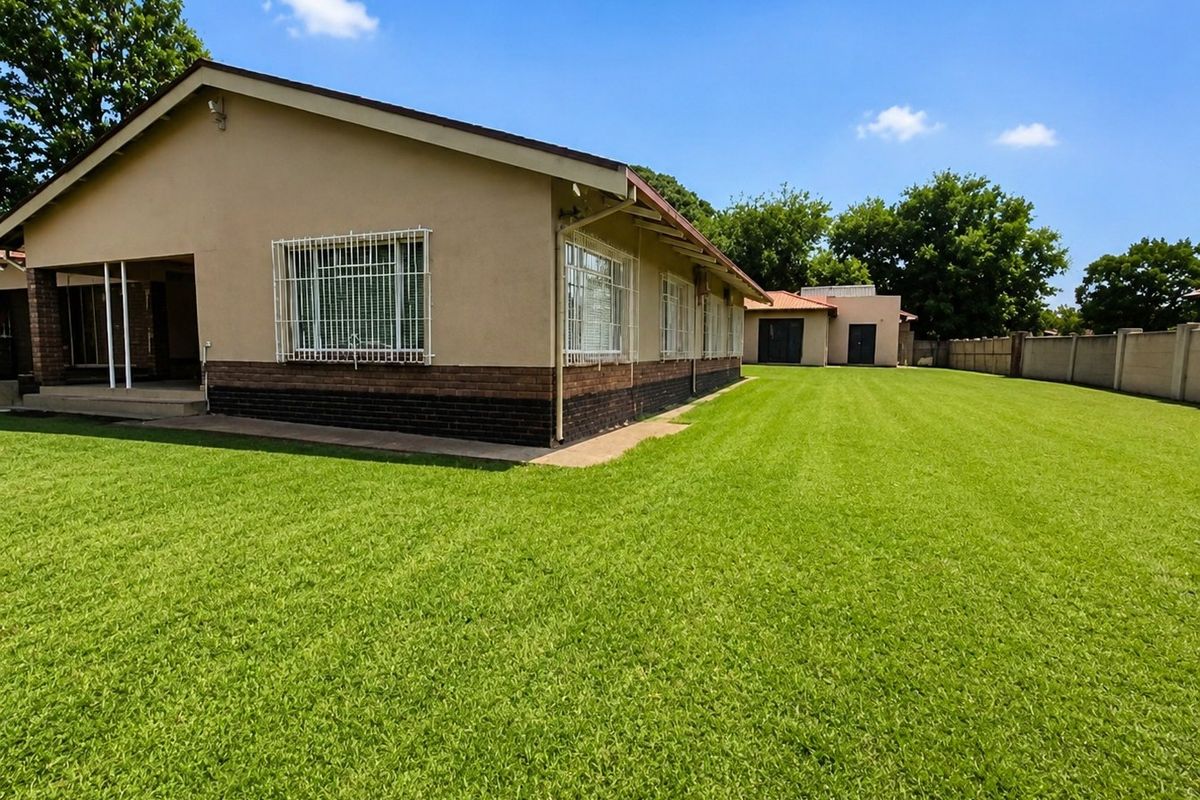A spacious rear garden featuring a well-maintained lawn, a covered patio area, and secure window bars on the main house structure.