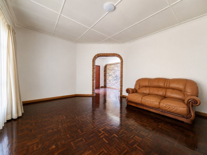 Spacious living room featuring polished parquet flooring, a distinctive brick archway leading to an adjacent area, and a classic panelled ceiling.