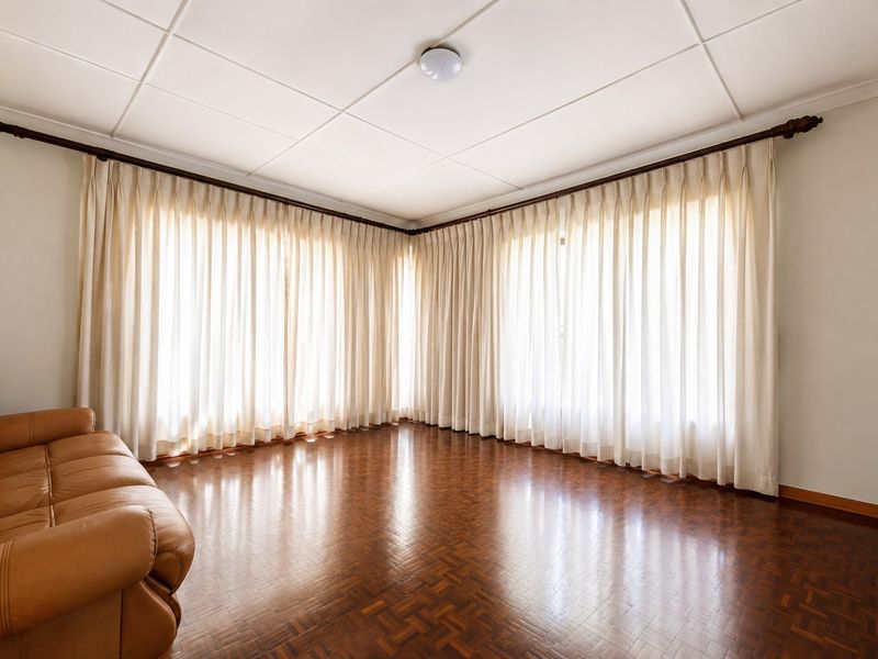 A spacious living room featuring classic parquet flooring, large windows with floor-to-ceiling curtains, and a tiled ceiling.