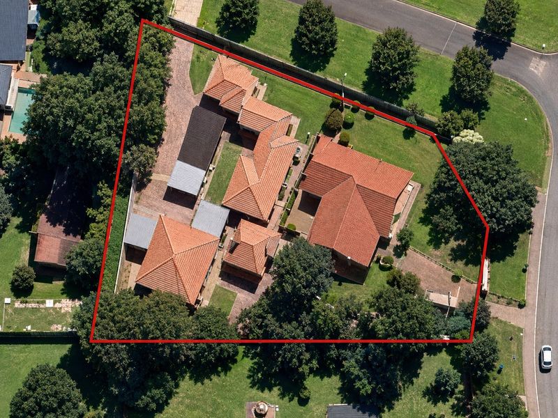 Aerial view of the property showcasing the main dwelling, outbuildings, paved driveway, and expansive landscaped garden within the defined boundary.