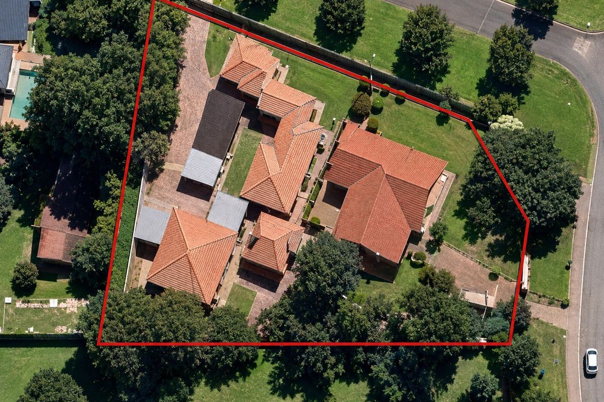 Aerial view of the property showcasing the main dwelling, outbuildings, paved driveway, and expansive landscaped garden within the defined boundary.