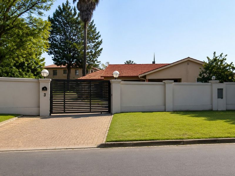 Front view of the property featuring a secure perimeter wall, sliding gate, paved driveway, and well-maintained lawn.