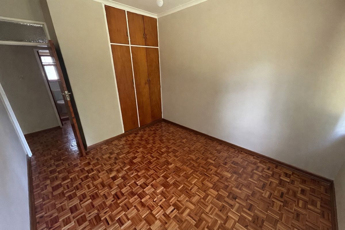 A vacant bedroom featuring classic parquet flooring and built-in wooden cupboards, offering a clean and neutral space ready for personalization.