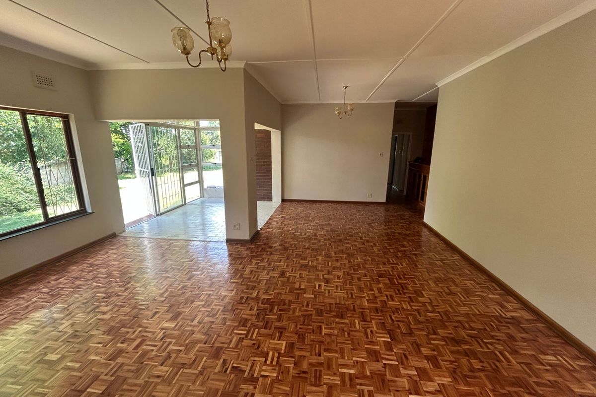 Spacious, empty living area featuring classic parquet flooring, neutral walls, and direct access to an outdoor patio through a security-fitted sliding door.