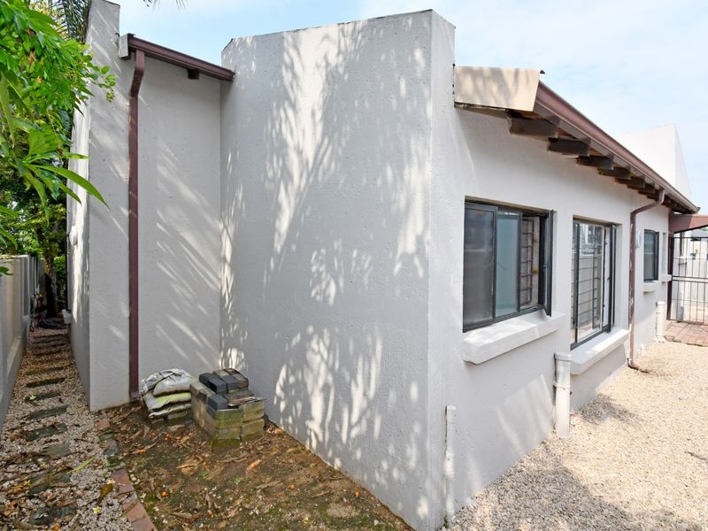 Rear exterior view of the cluster property showing painted masonry walls, metal window frames with security bars, and gravel ground cover.