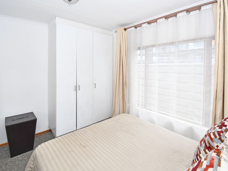 A functional bedroom featuring built-in cupboards, carpeted flooring, and a window fitted with security burglar bars.
