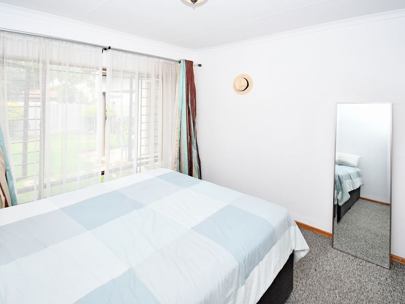 A functional bedroom featuring carpeted flooring, a large window with security bars, and neutral wall finishes.