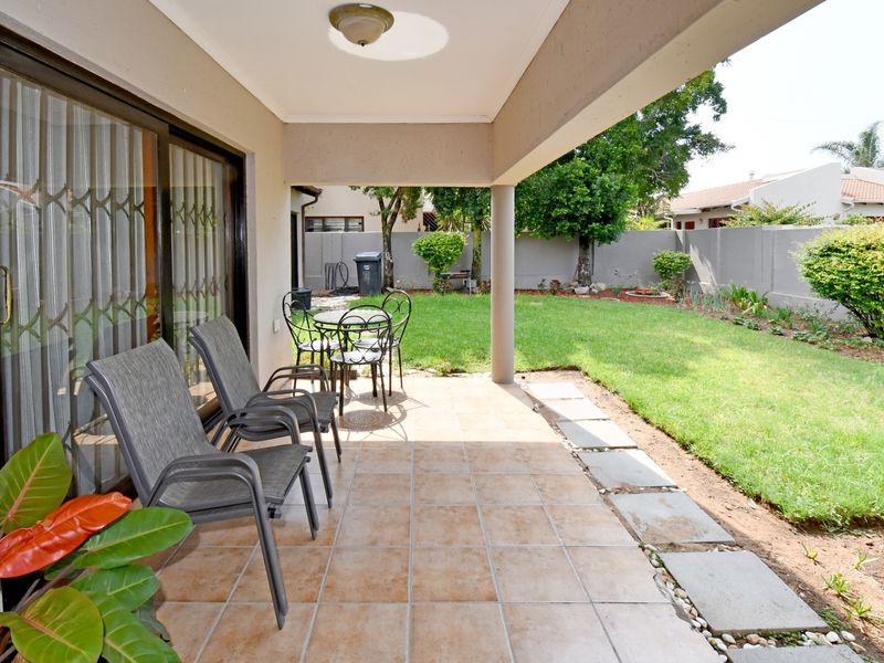 A covered patio area featuring tiled flooring and sliding door access, overlooking a private garden with boundary walling.