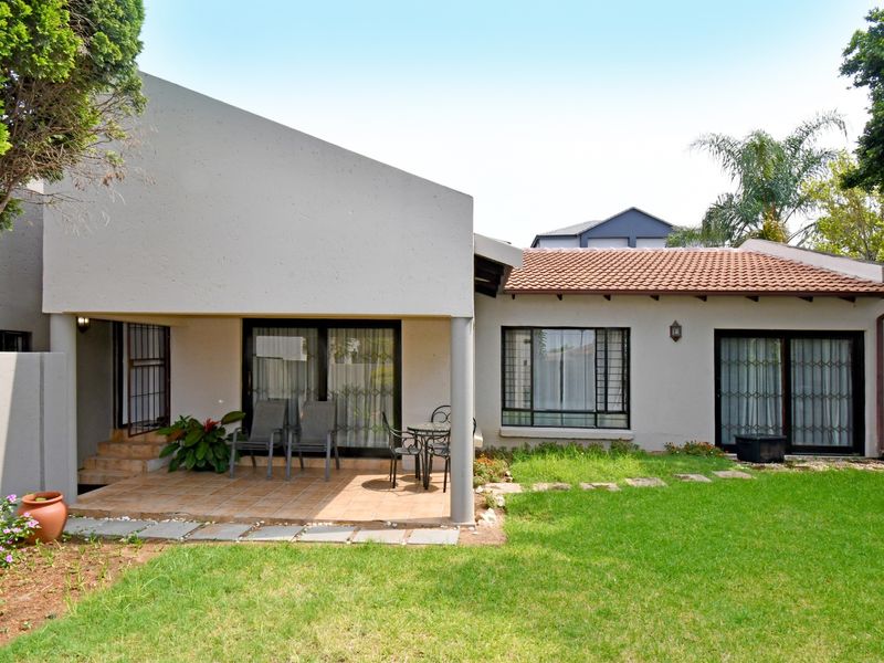 Rear view of the cluster property featuring a covered tiled patio, landscaped garden, and sliding door access to the interior living spaces.