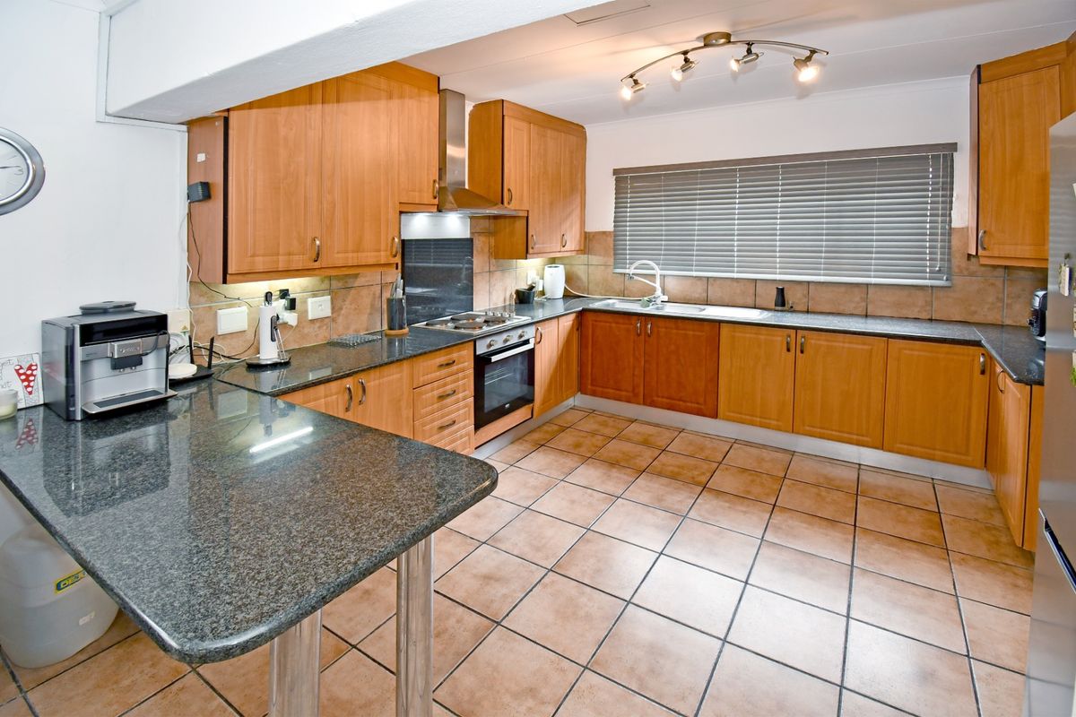 A functional kitchen featuring wooden cabinetry, granite countertops, a built-in oven with gas hob, and tiled flooring throughout.