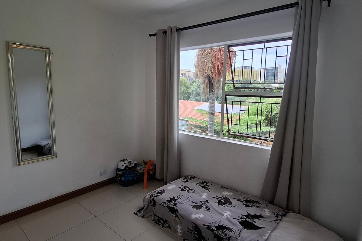 A bedroom featuring tiled flooring, security burglar bars on the window, and neutral wall finishes.