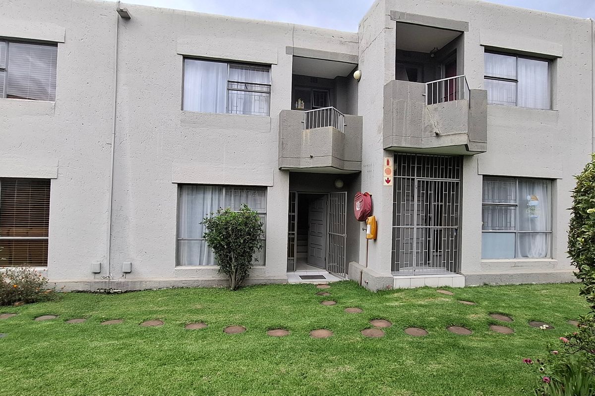 Rear view of a multi-story townhouse complex featuring concrete facade, security gates, and shared garden space.