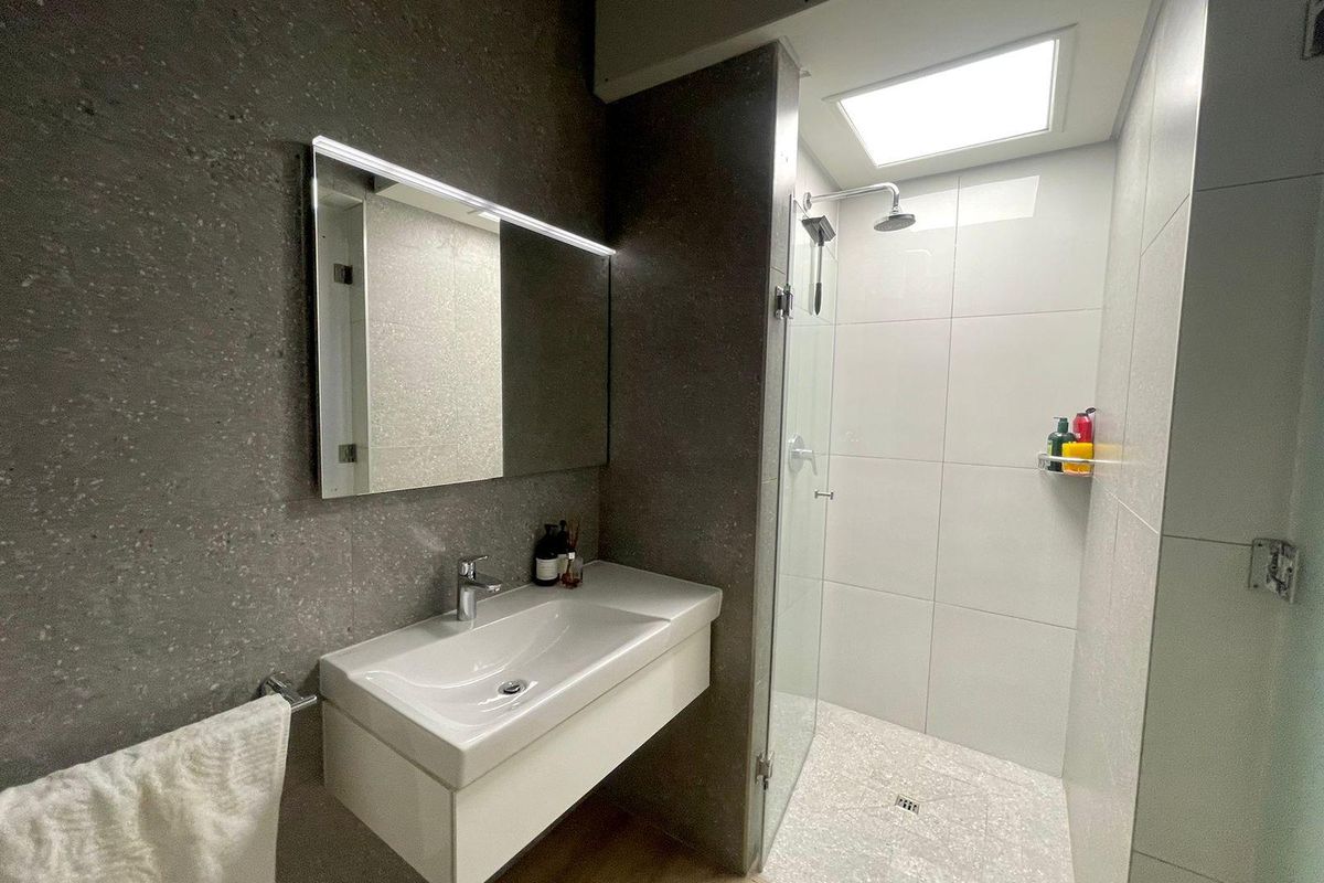 Modern bathroom featuring a wall-mounted vanity with integrated basin, backlit mirror, and a spacious walk-in shower with a skylight.
