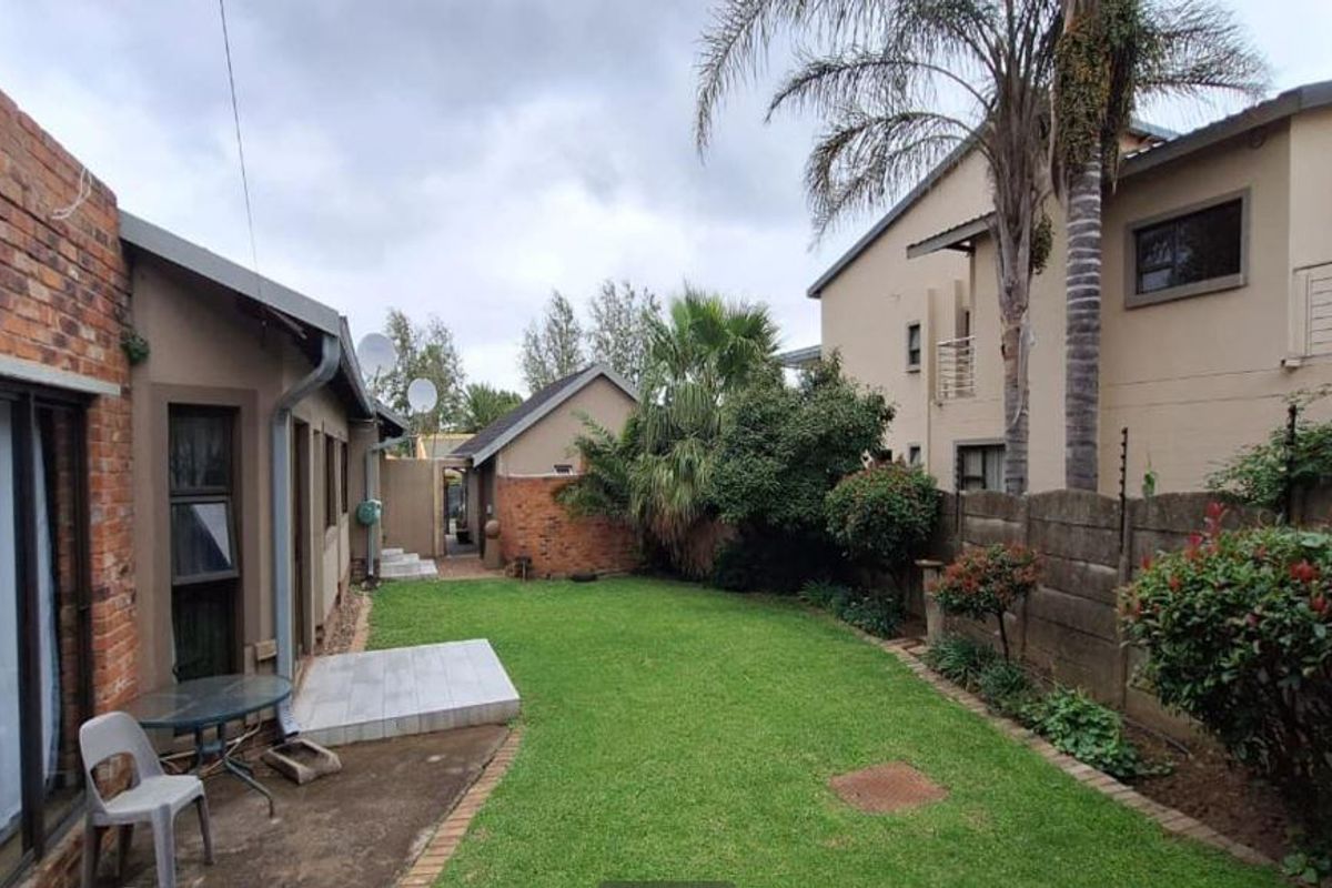 A rear garden view featuring a lawn, concrete patio area, and brick exterior walls with sliding door access to the main dwelling.