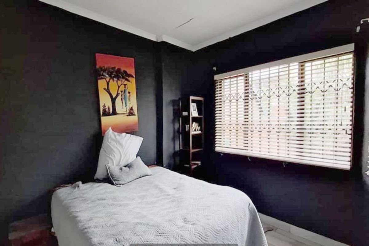 A bedroom featuring dark painted walls, fitted venetian blinds, and security bars on the windows.
