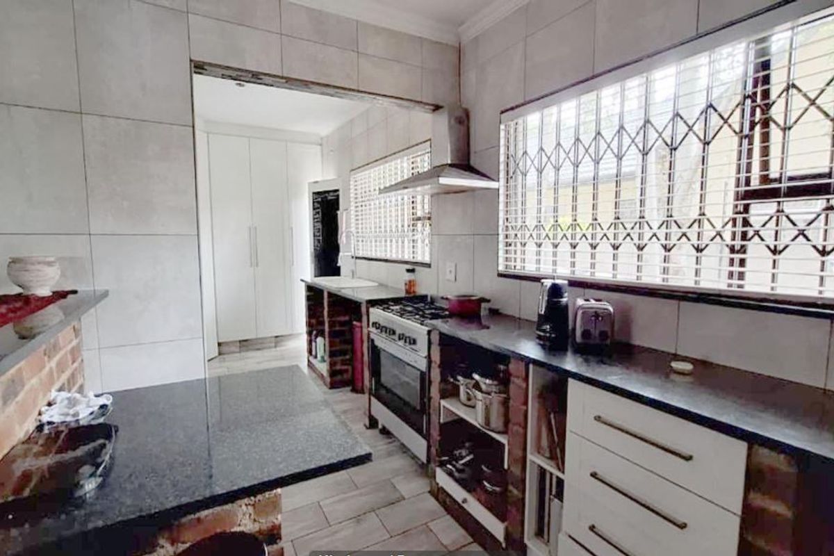 Functional kitchen featuring granite countertops, gas hob, extractor fan, and tiled wall finishes with integrated storage and security bars on windows.