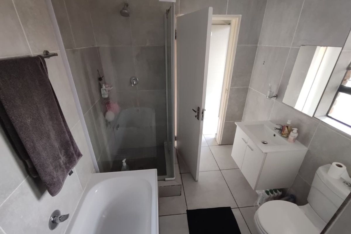 A modern bathroom featuring a separate bathtub and shower enclosure, a vanity basin, and neutral wall and floor tiling.