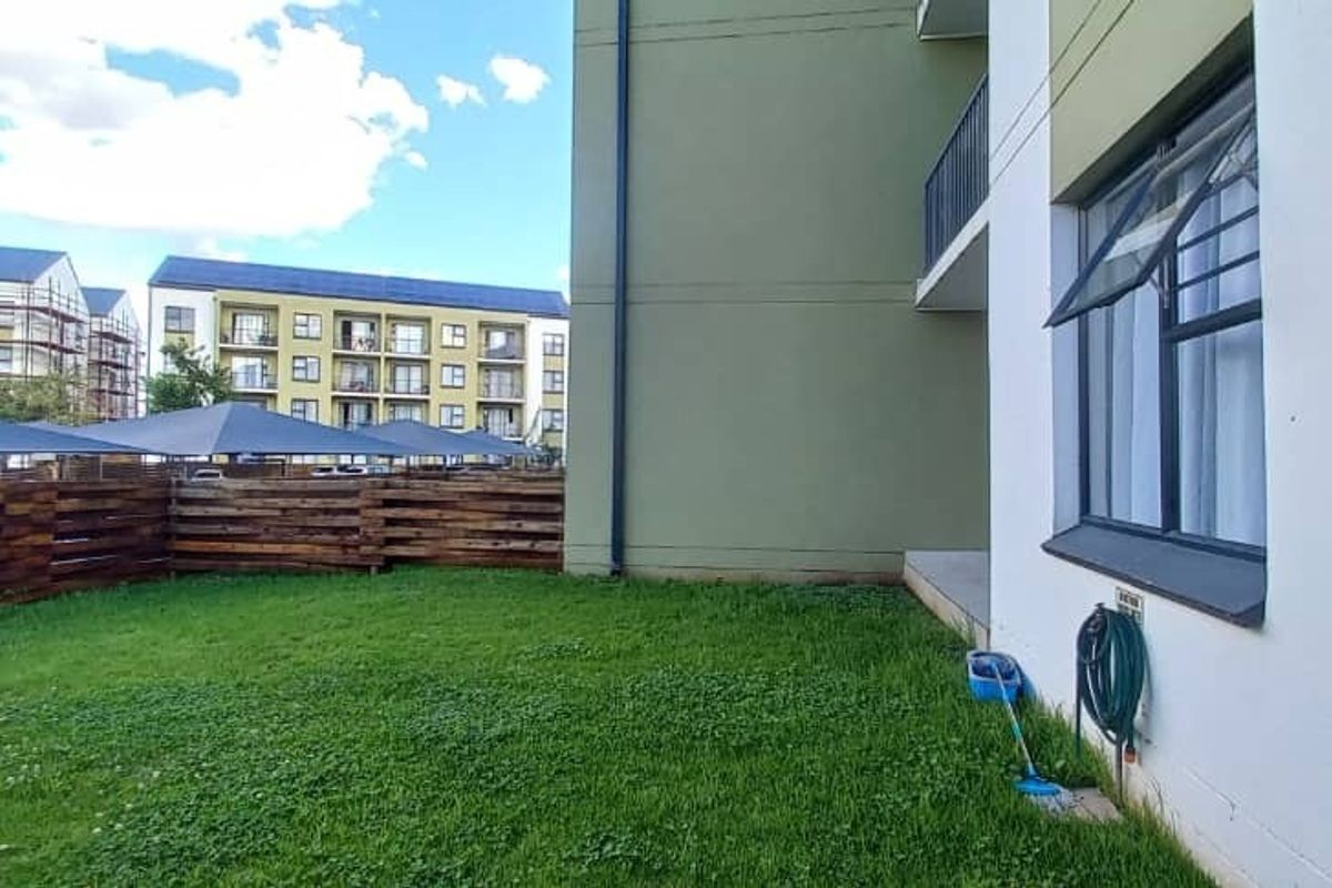 A ground floor apartment exterior featuring a private garden area, paved patio section, and secure perimeter fencing within a residential complex.