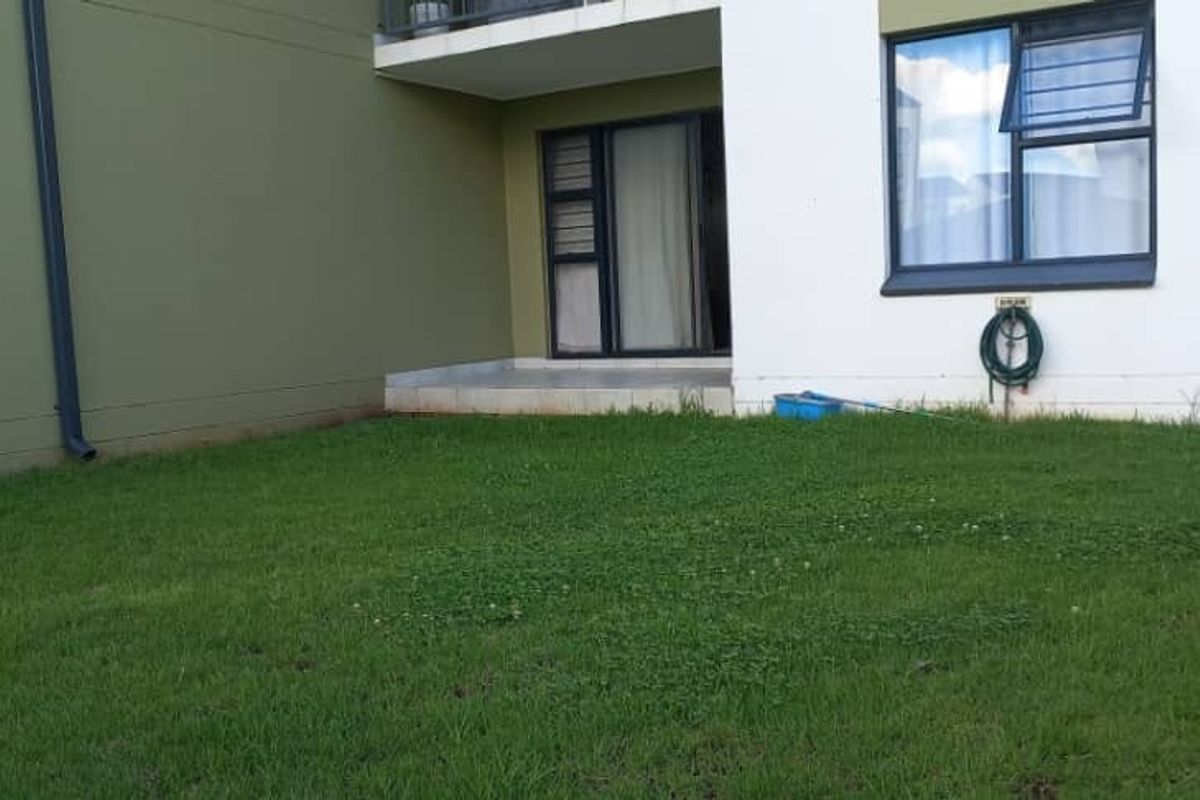 A rear view of the apartment featuring a small private lawn, a tiled patio area, and access via sliding glass doors.