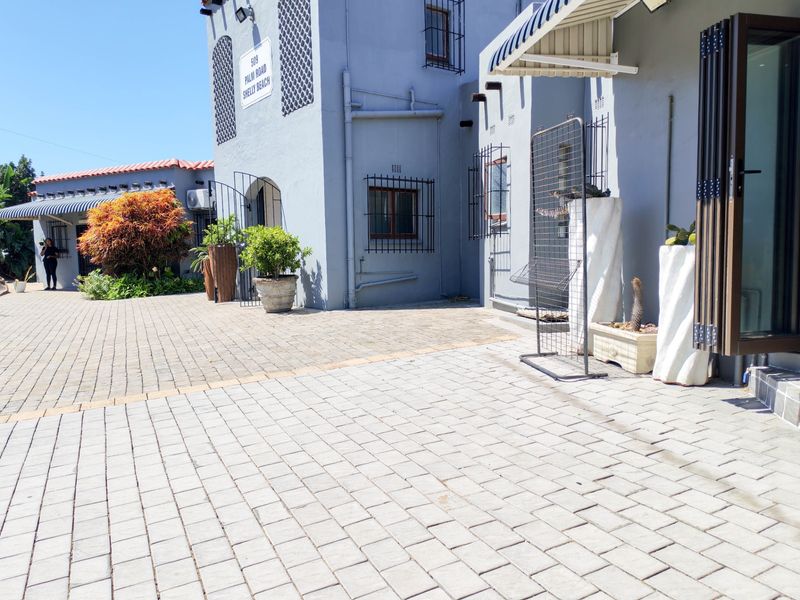 Front exterior view of a commercial property featuring paved driveway, security bars on windows, and folding glass doors under a shaded awning.