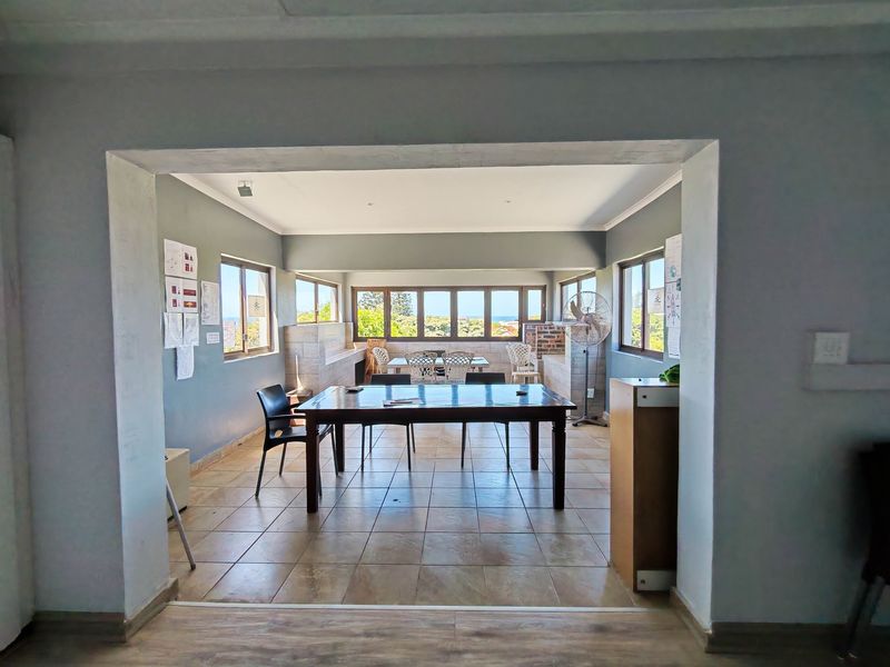 Open-plan commercial space featuring tiled flooring, large windows with natural light, and a built-in brick braai area, suitable for versatile office or dining use.
