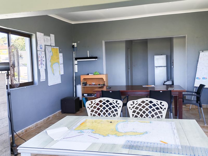 A functional office or training space featuring tiled flooring, neutral grey walls, and ample natural light through aluminium-framed windows.