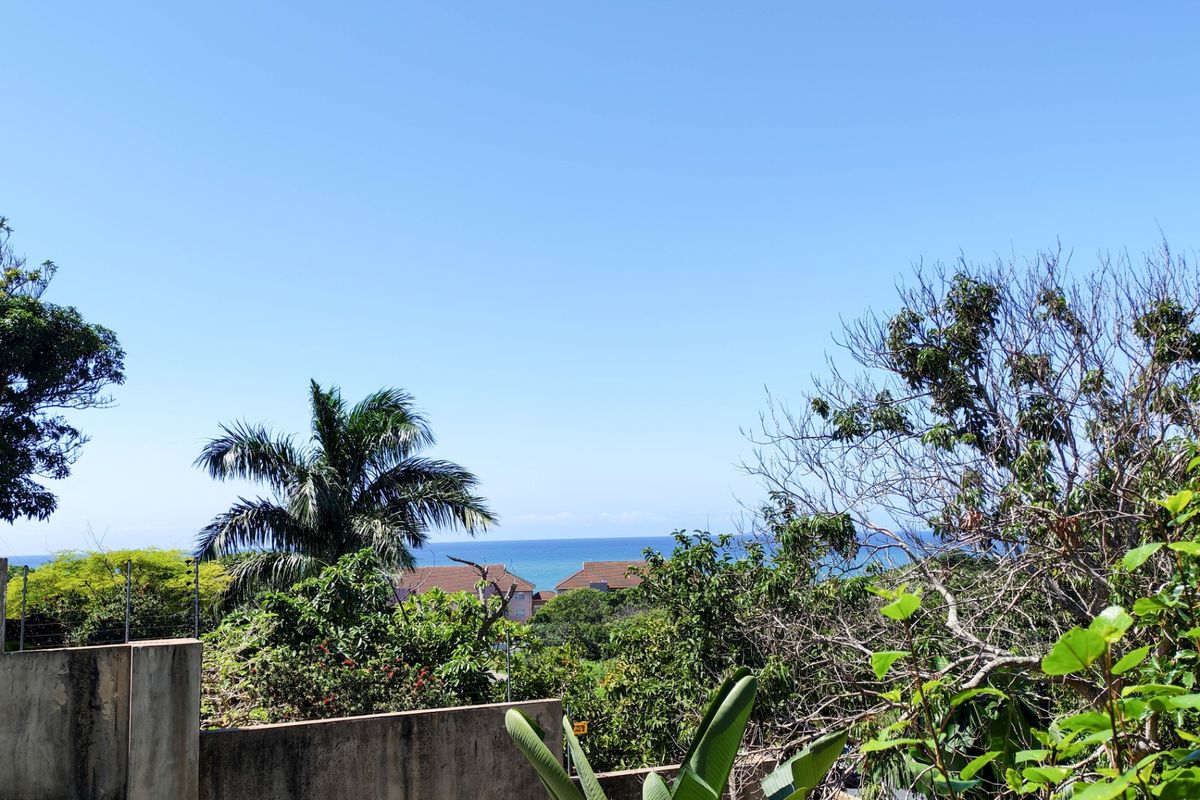A scenic view overlooking the ocean, framed by lush garden greenery and a concrete boundary wall.