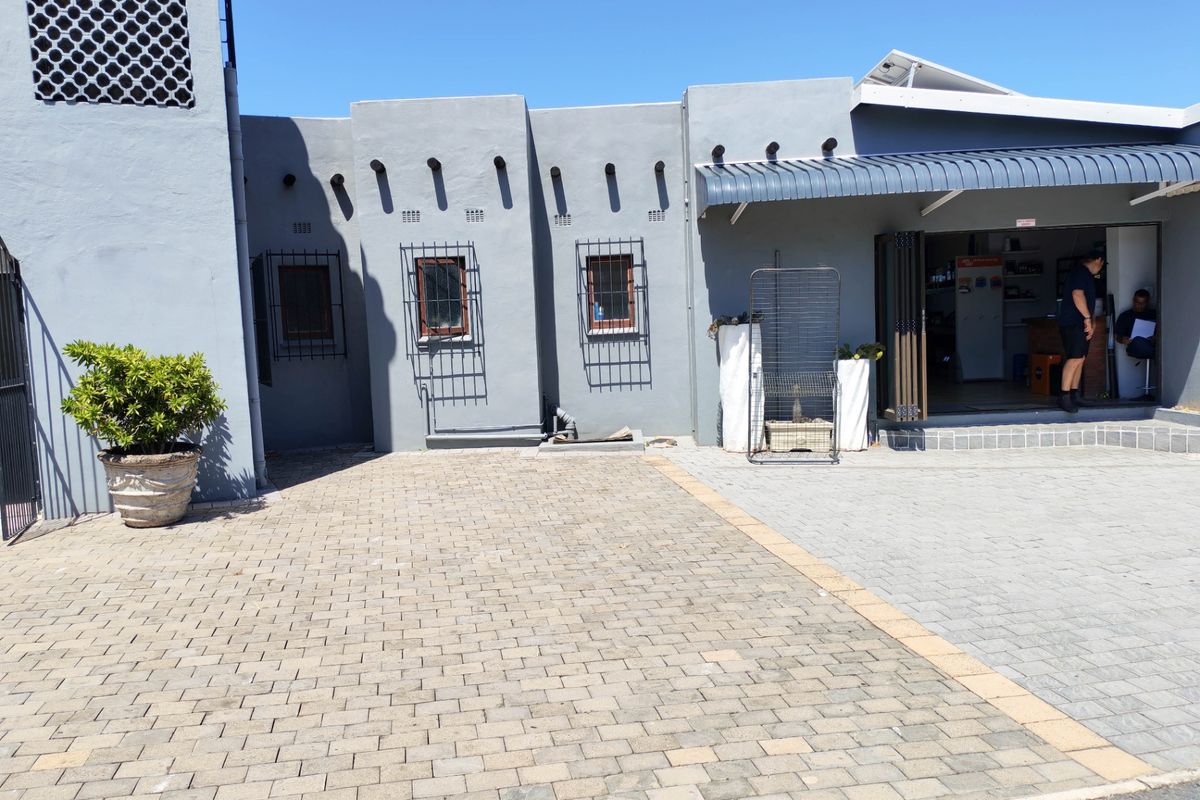 Rear exterior view of a commercial property featuring a paved courtyard, security-fitted windows, and a covered entrance area.