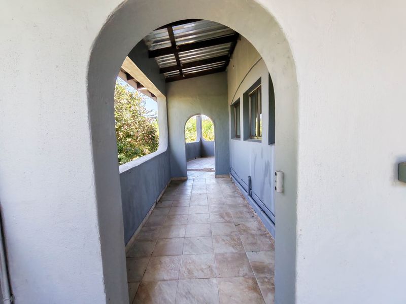 A covered outdoor balcony featuring arched architectural details, tiled flooring, and a corrugated metal roof structure.