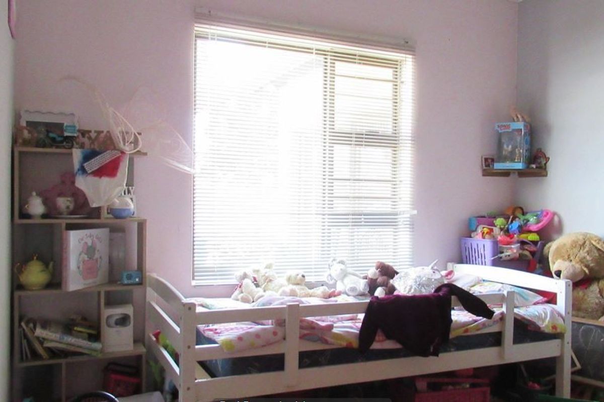 A standard bedroom featuring a window with fitted venetian blinds and security bars, providing natural light and basic security.