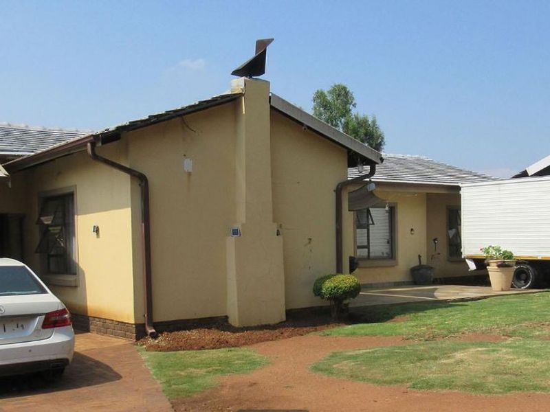 Front elevation of a single-story residential house featuring a tiled roof, brick chimney, and paved driveway access.