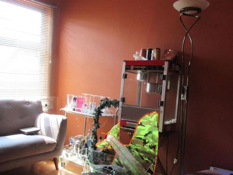 A living room space featuring orange walls and a window with venetian blinds, currently used as a casual entertainment area.
