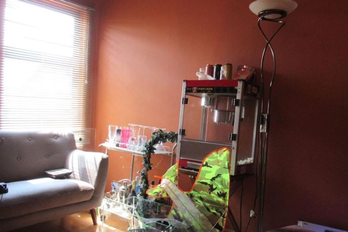 A living room space featuring orange walls and a window with venetian blinds, currently used as a casual entertainment area.