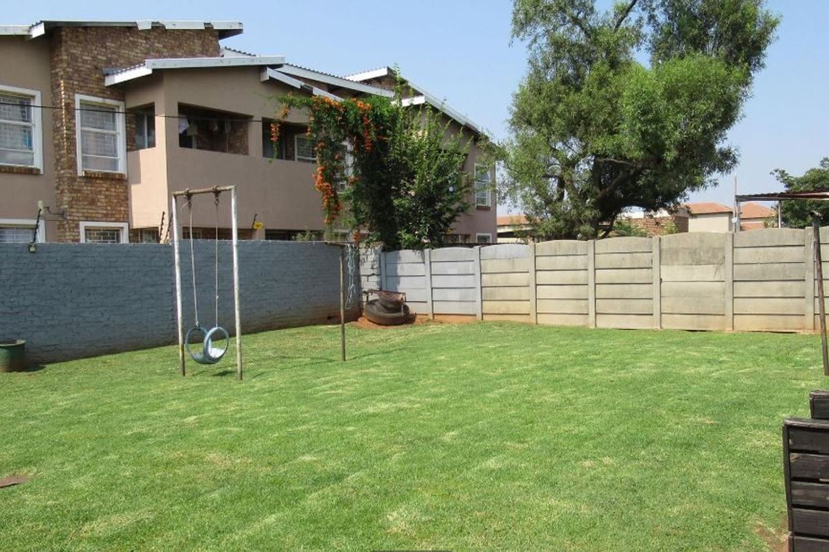 A private rear garden featuring a well-maintained lawn enclosed by a combination of painted brick and precast concrete boundary walls.