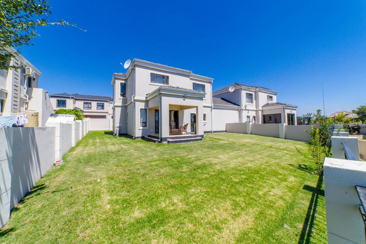 Rear view of a two-story residential property featuring a covered patio, a spacious lawn, and perimeter boundary walls.
