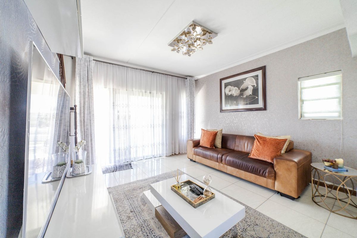 A bright and well-maintained living room featuring tiled flooring, a decorative ceiling light, and a large sliding glass door providing natural light.