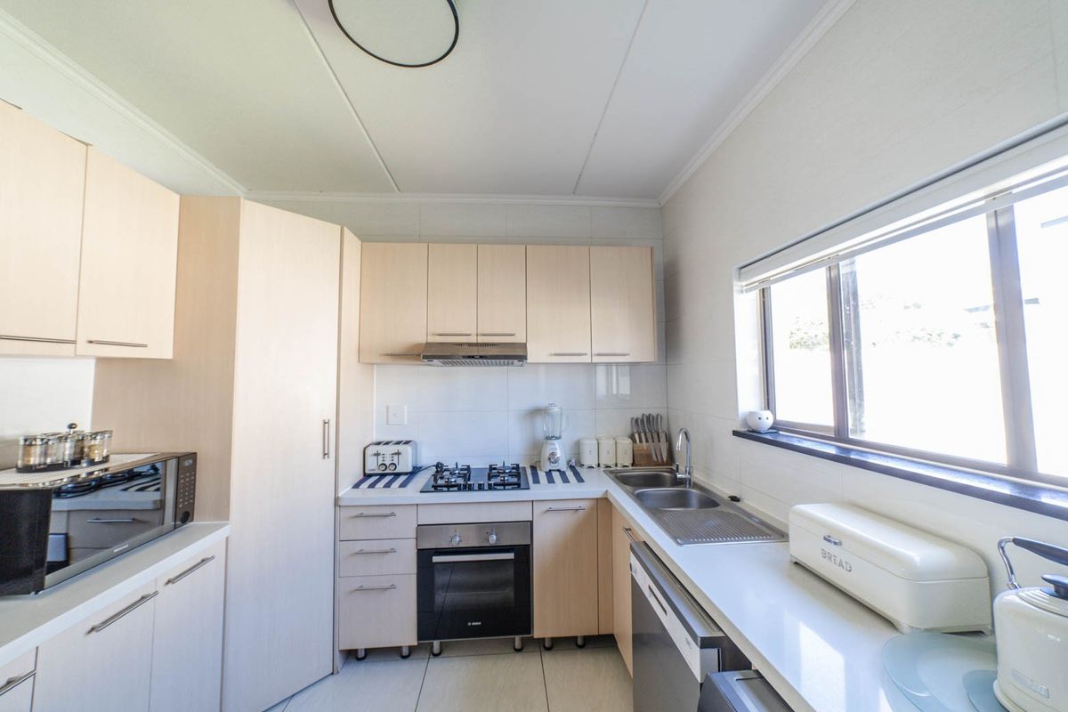 A functional kitchen featuring light wood cabinetry, a gas hob, built-in oven, extractor fan, and a double sink with a tiled backsplash.