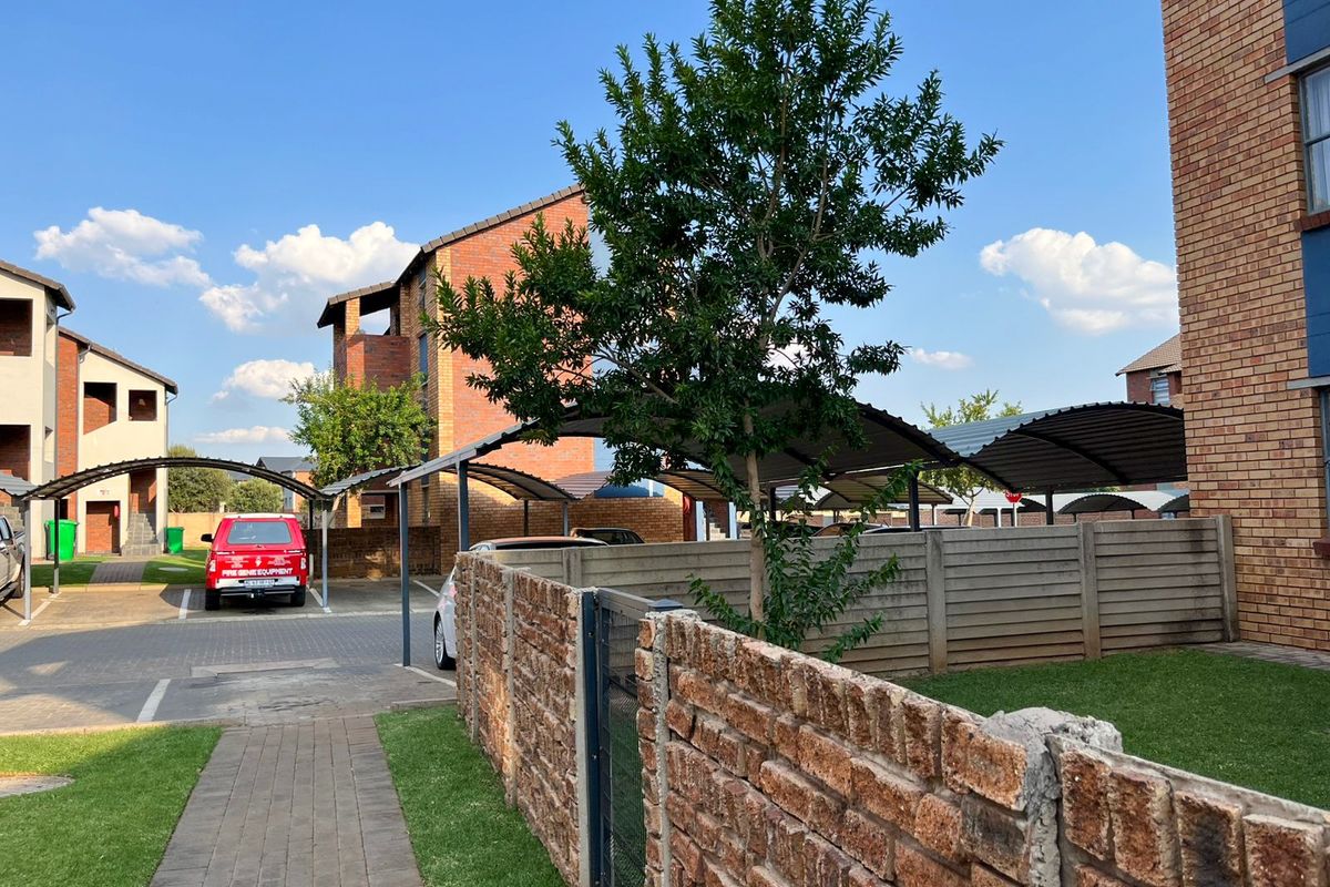 Exterior view of the apartment complex grounds featuring paved walkways, brick boundary walls, and covered carport parking bays.